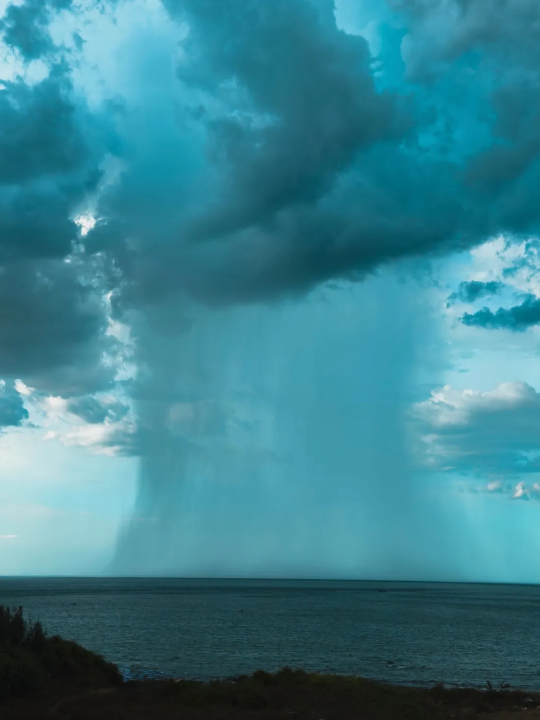 Starker Regenschauer unter einer dunklen Wolke über dem Meer